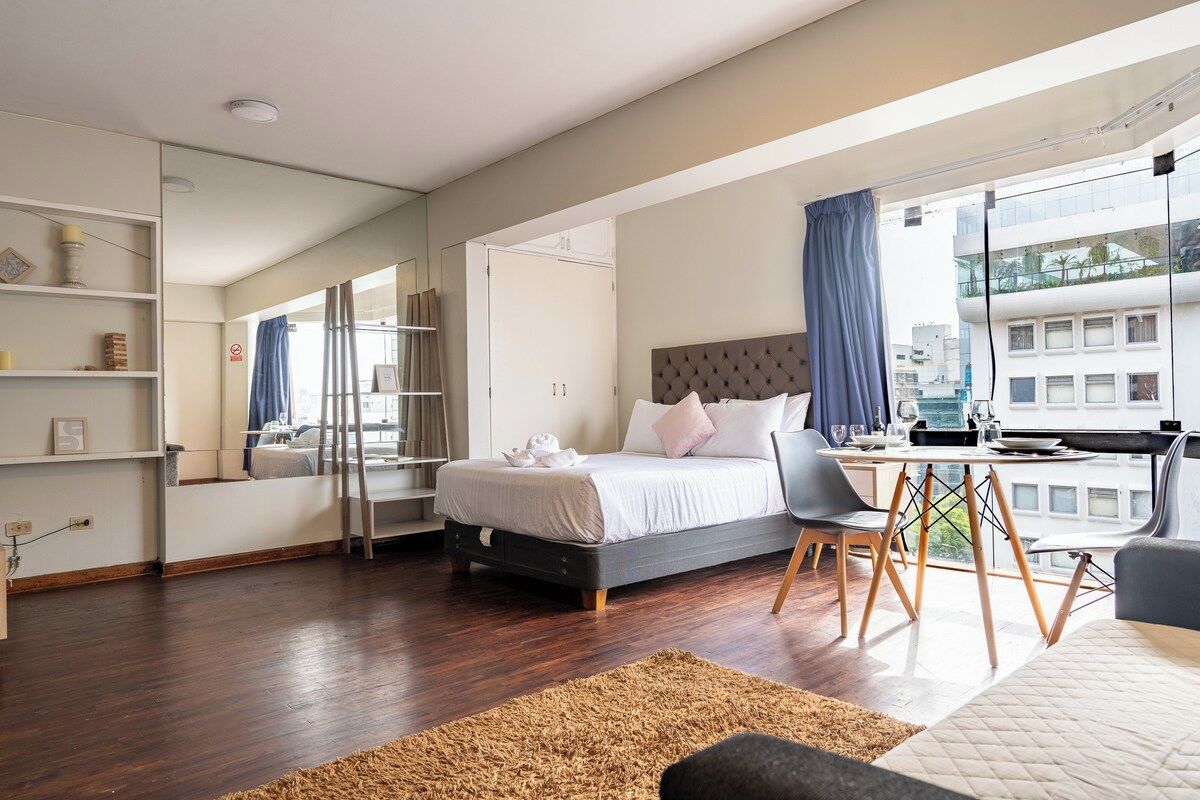 Un dormitorio moderno con cama, escritorio y un ventanal grande.