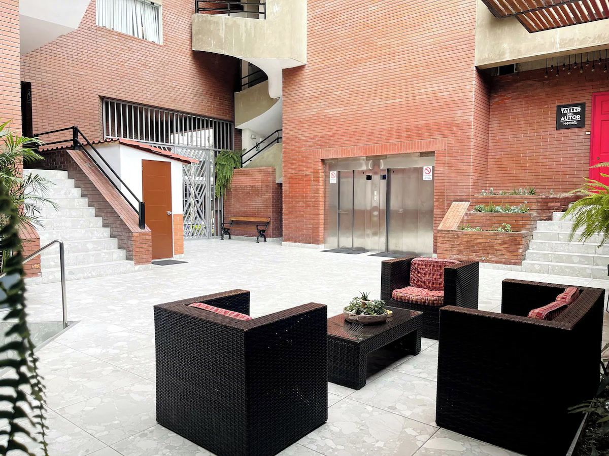 Un patio con mesas al aire libre, una escalera y una puerta roja.