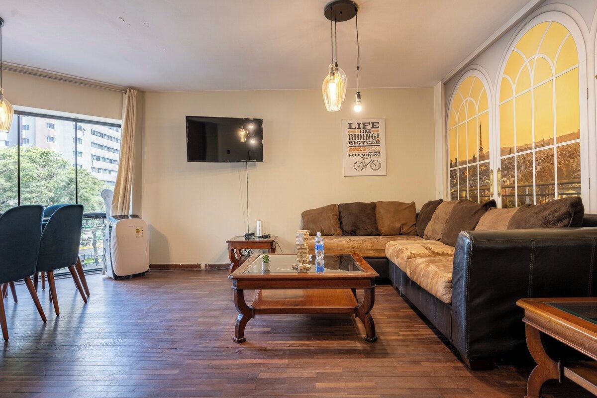 A living room with a sofa, chairs, a coffee table, a TV, and a window with a city view.