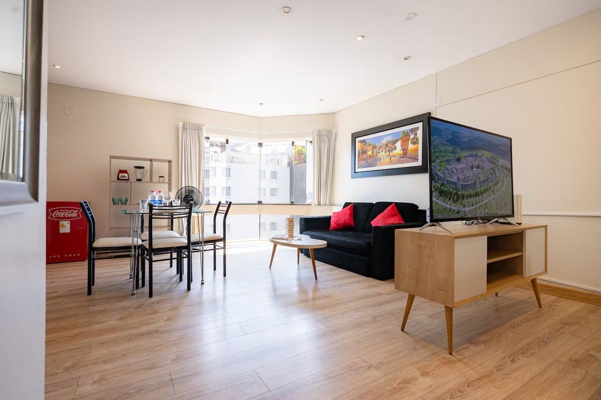 A modern living room with a dining area, a sofa, a coffee table, and a TV on a stand.