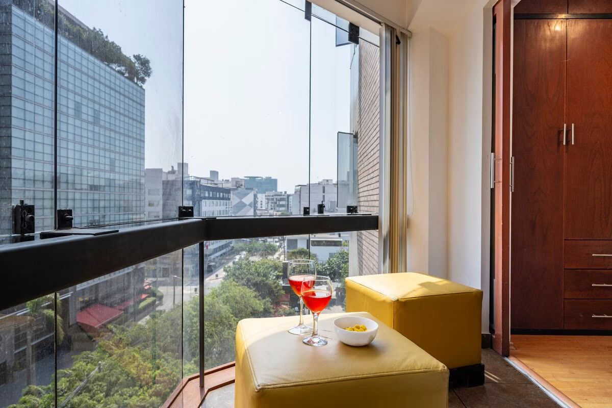 A balcony with a city view, a wooden door, and a yellow ottoman.