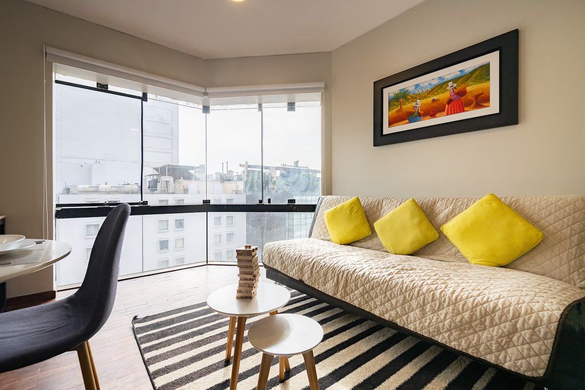 Un salon moderne avec un canapé, une table à manger et une chaise. Une grande fenêtre offre une vue sur les bâtiments à l’extérieur.