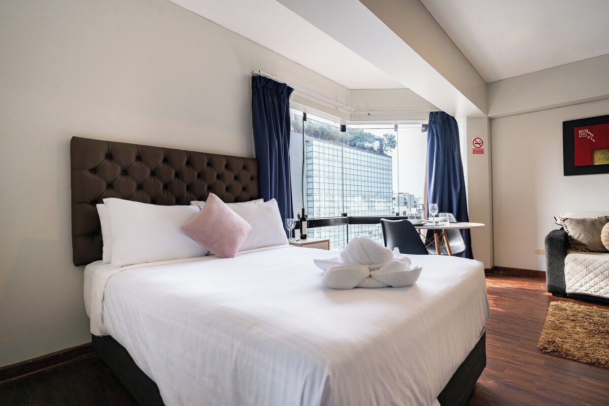 Habitación de hotel con una cama grande, un escritorio y vista a un edificio desde la ventana.