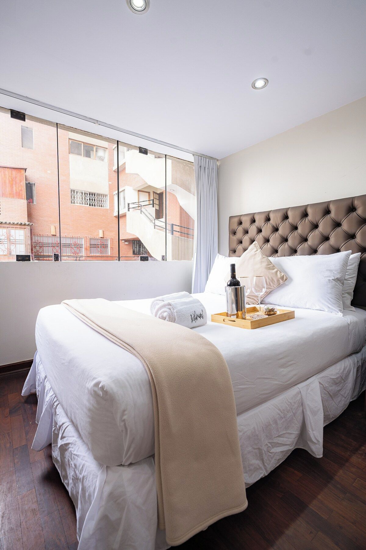 Habitación de hotel con una cama grande, vistas al exterior y una bandeja con una botella y vasos.