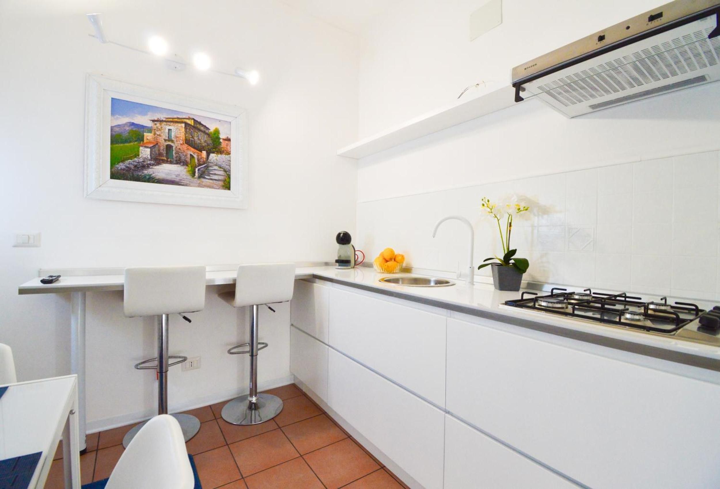 Una cocina moderna con armarios blancos, estufa a gas, lavabo y un taburete de bar.