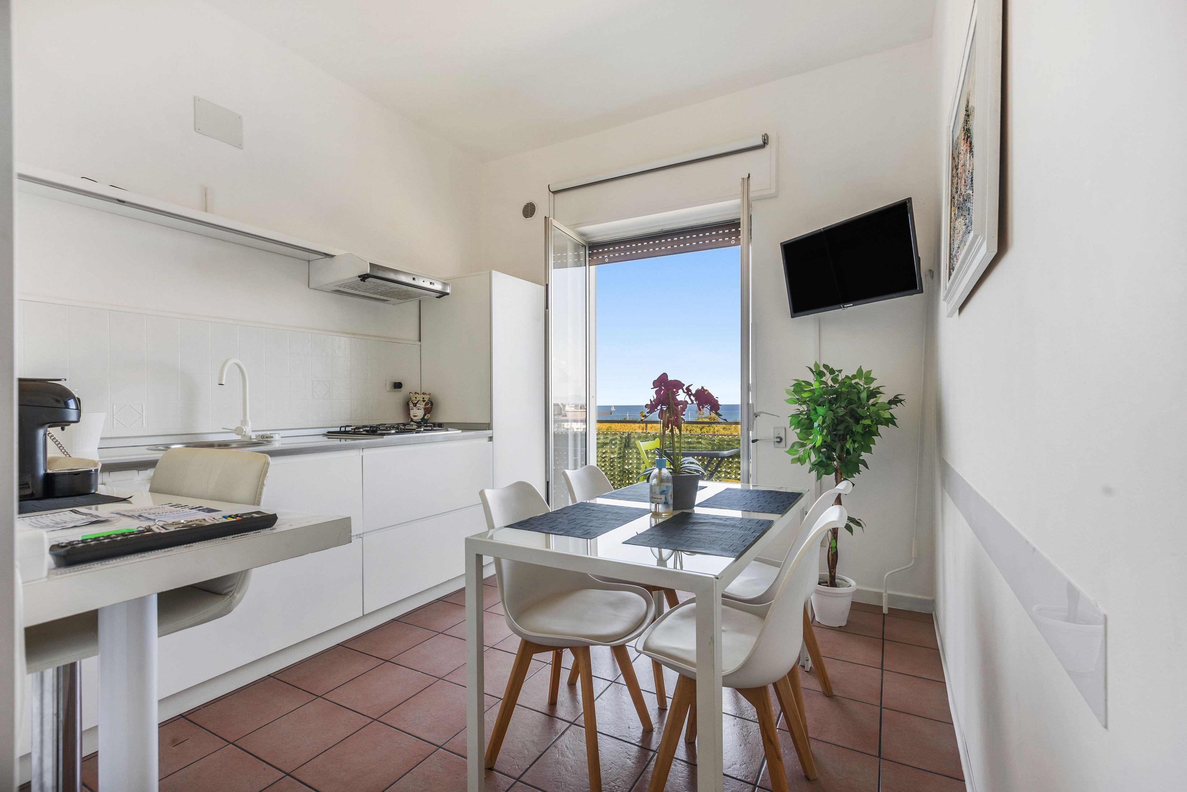 Une cuisine moderne avec un coin repas, un téléviseur fixé au mur et une vue sur la mer par la fenêtre.