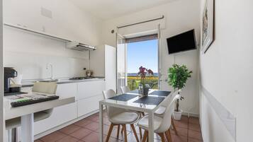 Une cuisine moderne avec un coin repas, un téléviseur fixé au mur et une vue sur la mer par la fenêtre.