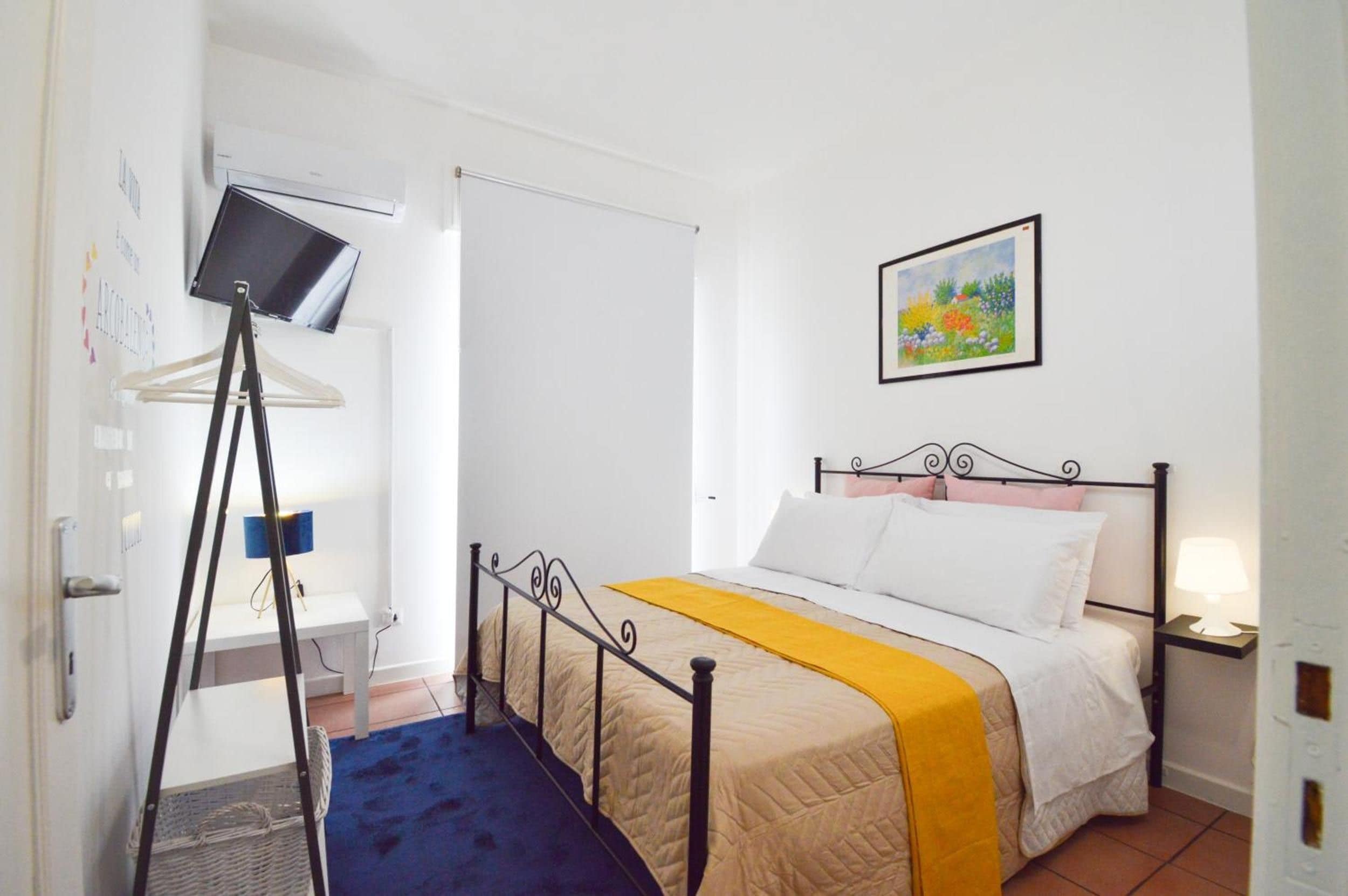 Un dormitorio con cama, escritorio con lámpara, un cuadro en la pared y una ventana.