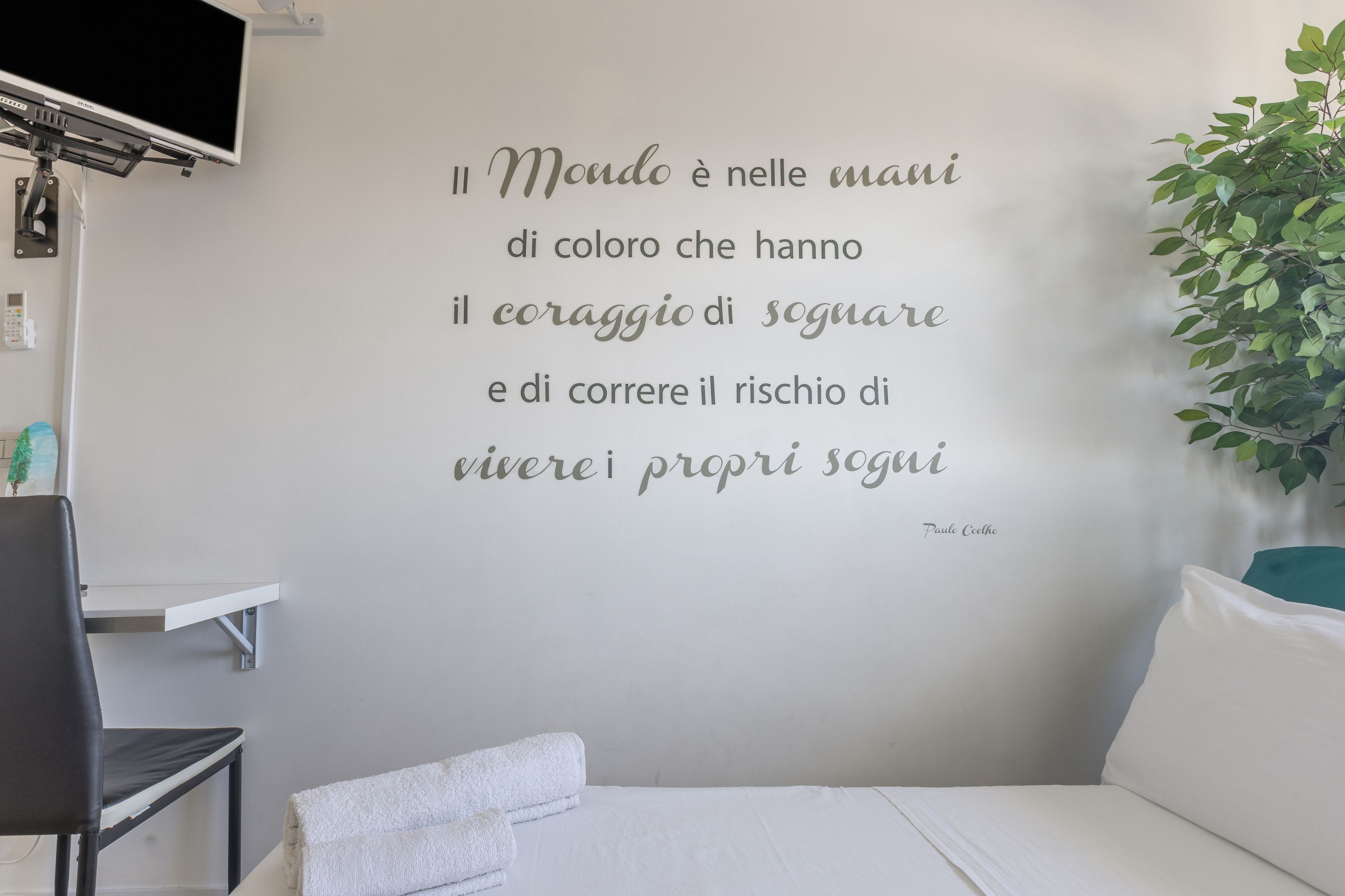 A bedroom with a white wall featuring a quote in Italian.