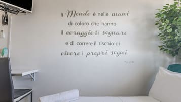 A bedroom with a white wall featuring a quote in Italian.