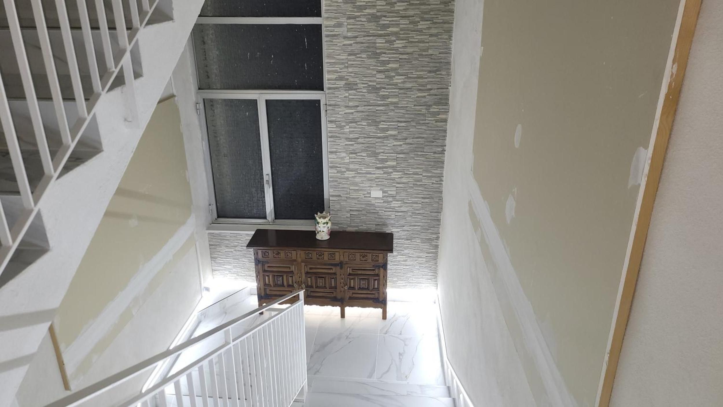 Eine Treppe führt zu einem Raum mit einem dekorativen Schrank und einem Fenster mit einer strukturierten Wand.