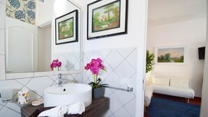 A bathroom with a white sink, two framed landscape paintings, a mirror, and a white bench in the adjacent room. - Apartment 'Ekaterina House 2 Minuti Dal Mare' (Brolo)