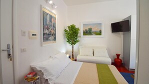 A hotel room with a bed, a TV, a painting, a plant, and a red vase. - Apartment 'Ekaterina House 2 Minuti Dal Mare' (Brolo)