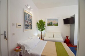 Ein Hotelzimmer mit einem Bett, einem Fernseher, einem Gemälde, einer Pflanze und einer roten Vase.