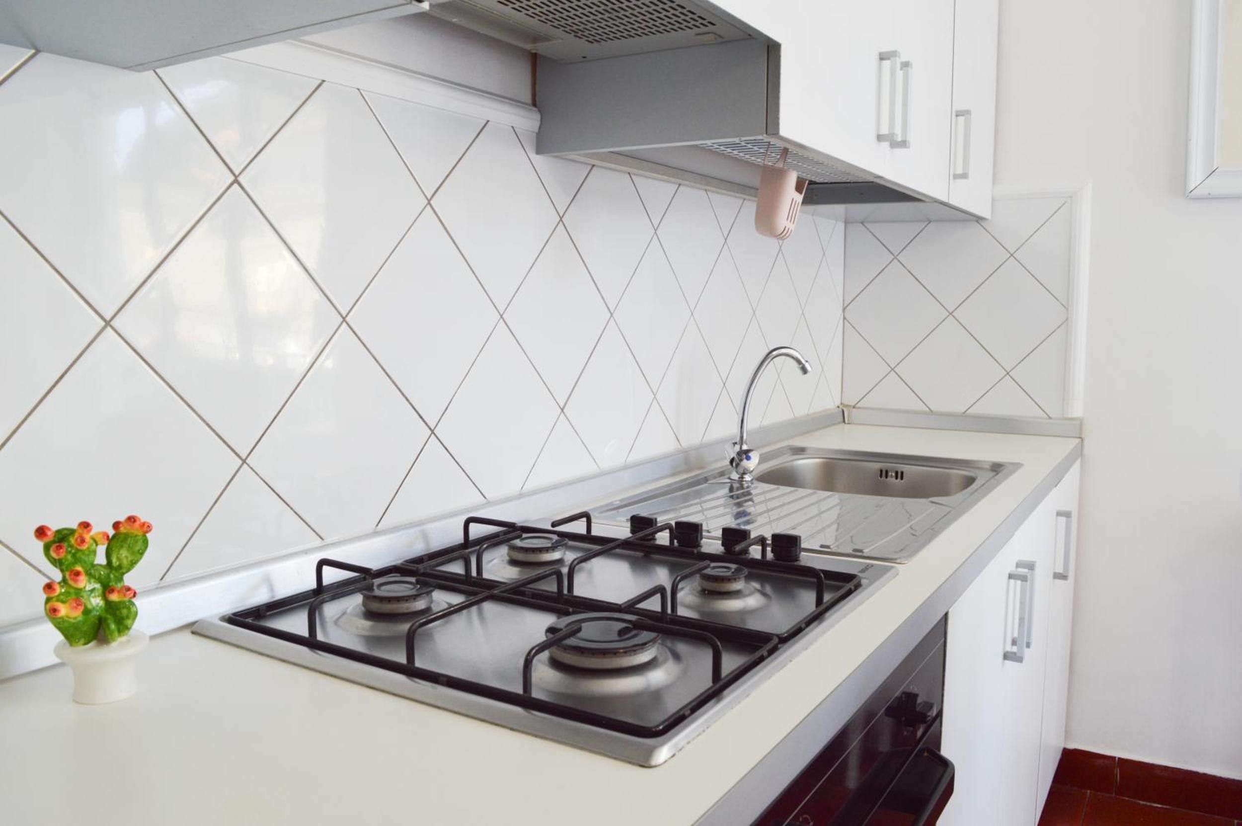 Une cuisine moderne équipée d’une cuisinière à gaz, d’un évier en acier inoxydable et d’un dosseret de carrelage blanc.