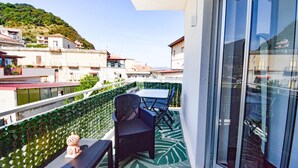 A balcony with a table and chairs, a decorative item, and a view of a hillside with buildings. - Apartment 'Ekaterina House 2 Minuti Dal Mare' (Brolo)