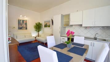 A compact living space with a kitchenette, a dining area with a table and chairs, a sofa, and a small plant.