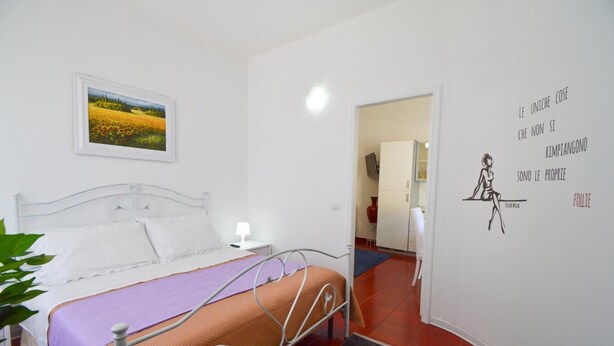 A bedroom with a bed, a bedside table, a lamp, a wall with a quote, and a door leading to another room. - Apartment 'Ekaterina House 2 Minuti Dal Mare' (Brolo)