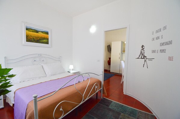Ein Schlafzimmer mit einem Bett, einem Nachttisch, einer Lampe, einer Wand mit einem Zitat und einer Tür zu einem anderen Raum.