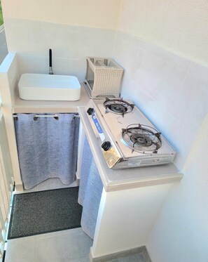 A compact kitchen with a white sink, a gas stove, and a laundry basket.