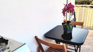 Uma pequena área de refeições ao ar livre com mesa, cadeiras, fogão a gás e um vaso de plantas com flores.