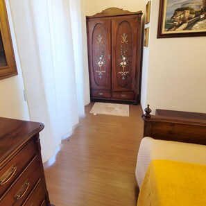 A room with a wooden wardrobe, a bed with a yellow bedspread, and a painting on the wall.