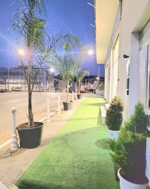 A hotel entrance with a paved pathway, potted plants, and a building facade.