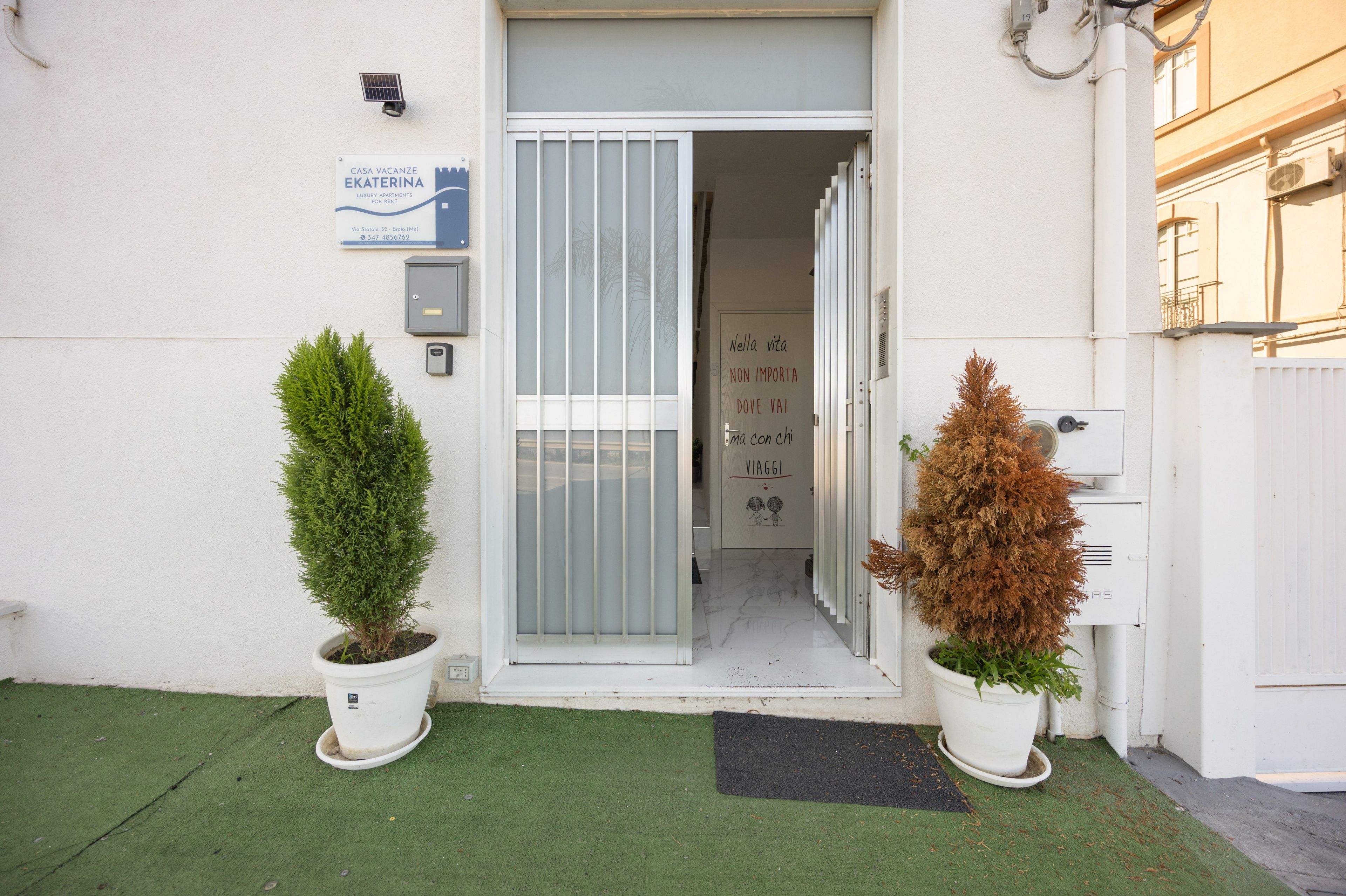 Een gebouwtoegang met een deur, een brievenbus en twee plantenpotten.