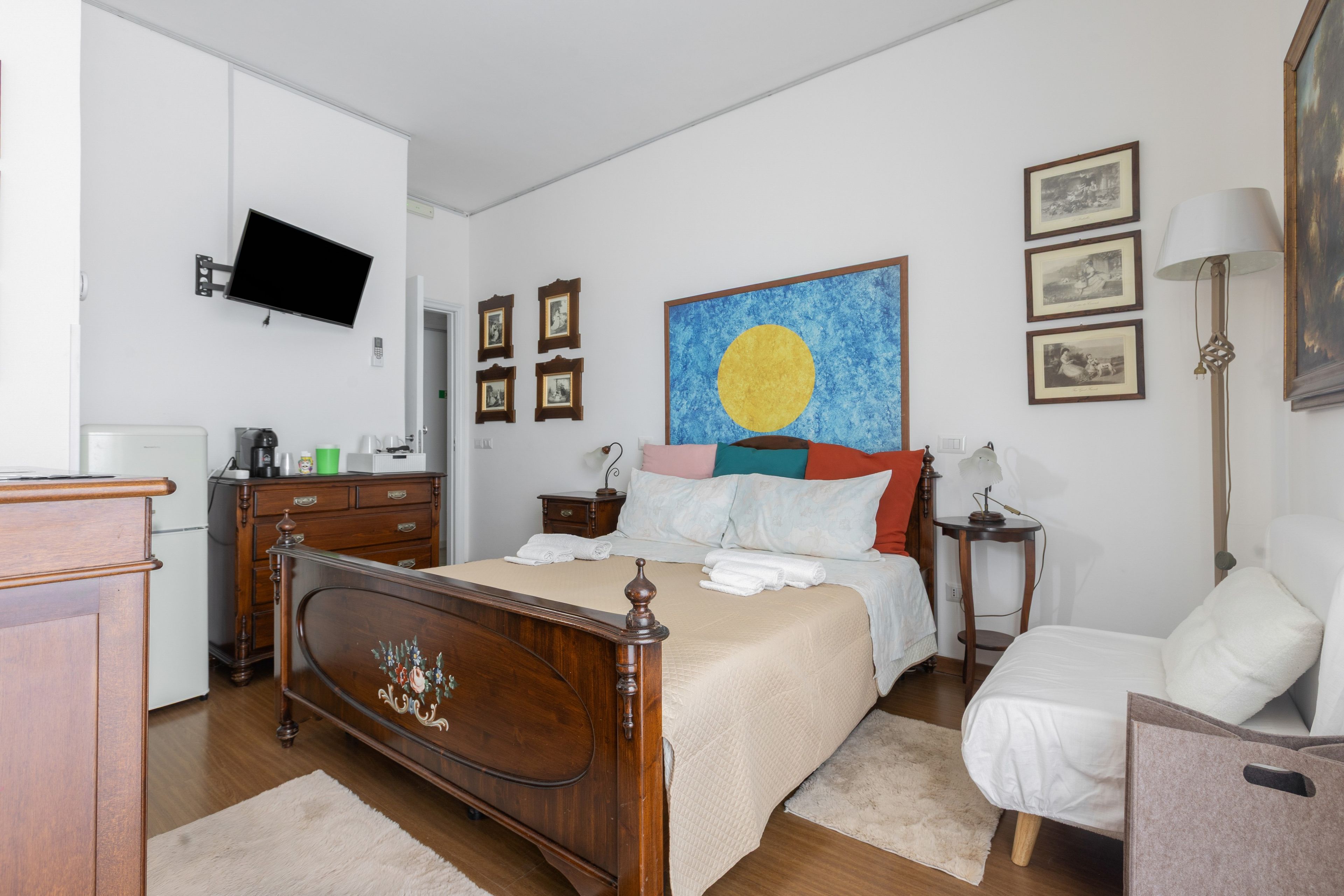 Ein Hotelzimmer mit einem hölzernen Bett, einem Flachbildfernseher, einem Gemälde und einem Schreibtisch mit Lampe.