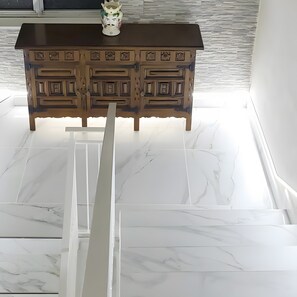 A wooden cabinet with intricate carvings, a white marble floor, and a white vase on top.