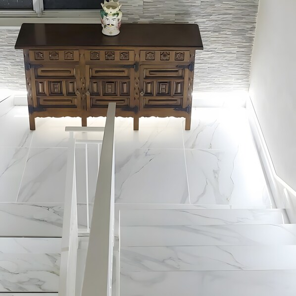 A wooden cabinet with intricate carvings, a white marble floor, and a white vase on top.