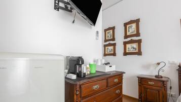 A room with a white radiator, a coffee maker, a cabinet, and framed pictures on the wall.