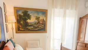 Quarto bem arrumado com cama, mesa de cabeceira, abajur e um quadro na parede.