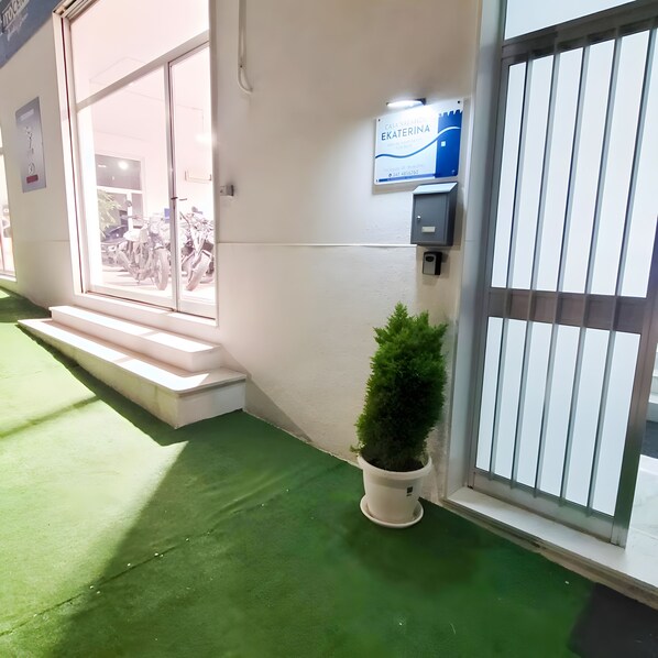 A building entrance with a sign, a potted plant, and steps leading to a door.