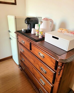 A kitchenette with a coffee maker, cups, a kettle, and a box of bread.