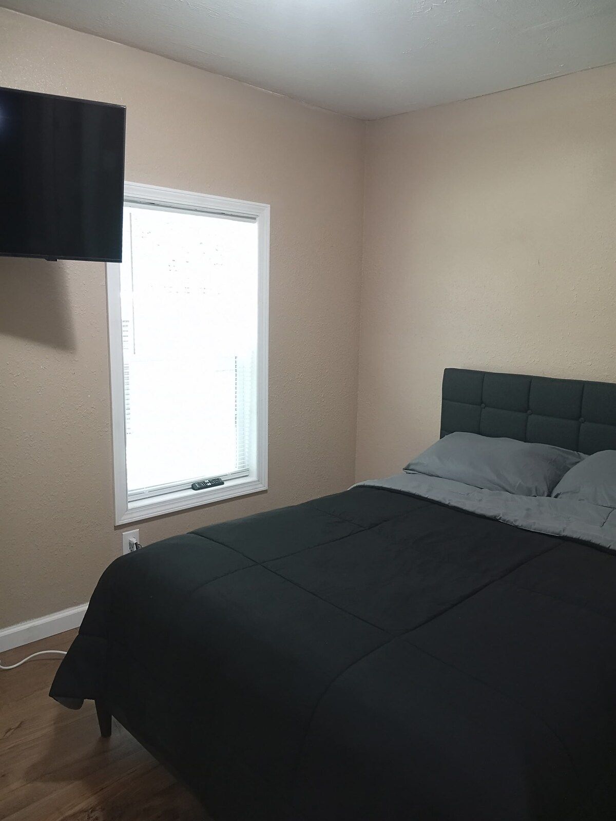 A bedroom with a bed, a window with blinds, and a wall-mounted television.