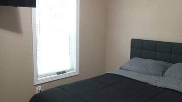A bedroom with a bed, a window with blinds, and a wall-mounted television.