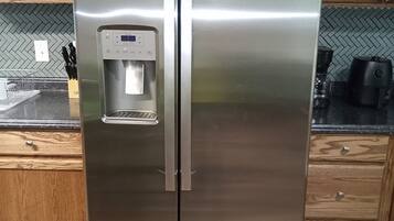 Un refrigerador de acero inoxidable con dispensador de agua, ubicado en una cocina con armarios de madera y salpicadero de baldosas tipo herringbone.