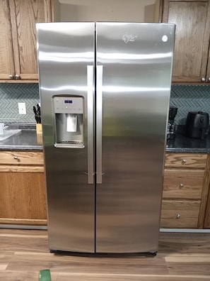 A stainless steel refrigerator with a water dispenser, located in a kitchen with wooden cabinets and a herringbone tile backsplash.
