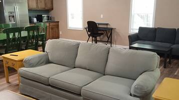 Una sala de estar con sofá, una mesa de comedor, una zona de cocina con armarios y electrodomésticos, y un ventanal.
