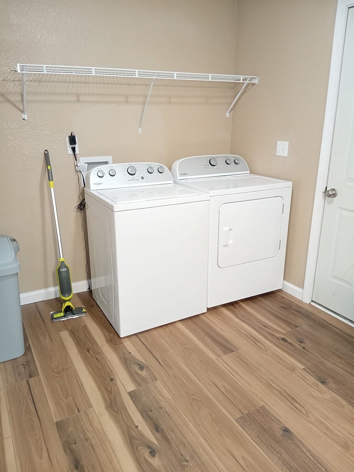 A laundry room with two white Whirlpool washers and dryers, a mop, and a metal drying rack.