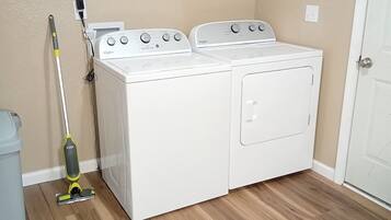 A laundry room with two white Whirlpool washers and dryers, a mop, and a metal drying rack.