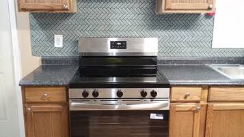 Una cocina con armarios de madera, estufa de acero inoxidable y un salpicadero con motivo de espiga.