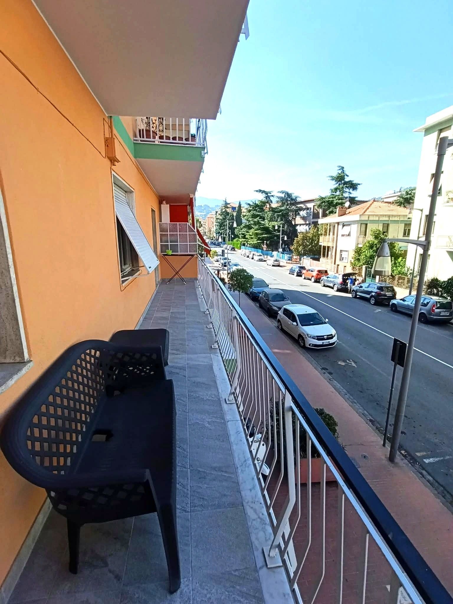 Un balcone con una panchina, un corrimano e vista su una strada con auto parcheggiate.