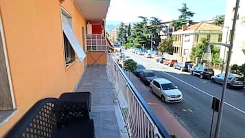 Un balcone con una panchina, un corrimano e vista su una strada con auto parcheggiate.