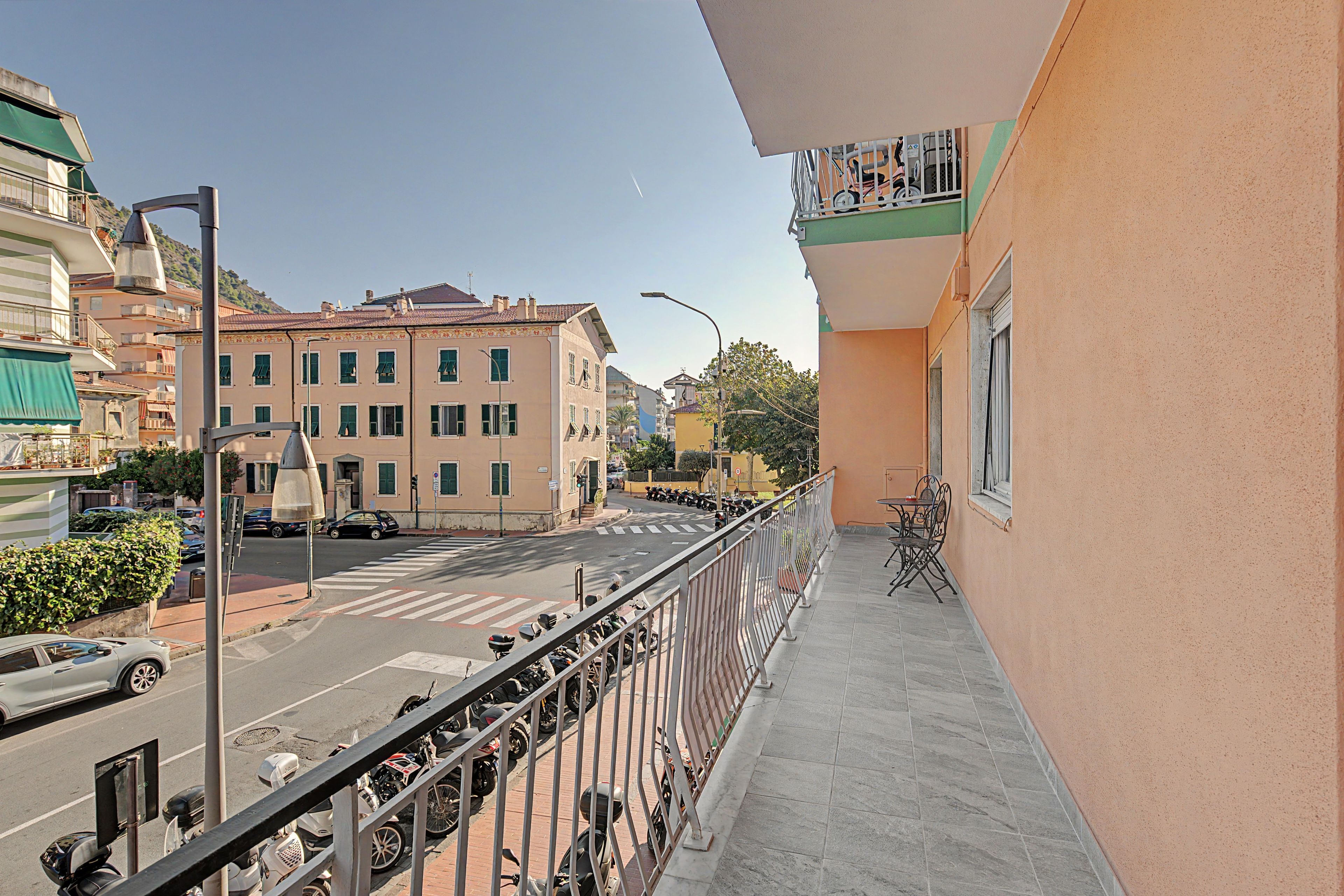 Un balcone con vista su una strada, uno scooter parcheggiato e un edificio con numerose finestre.