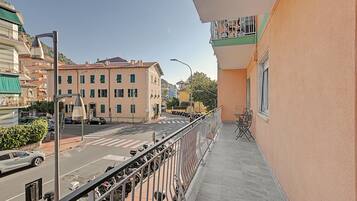 Un balcone con vista su una strada, uno scooter parcheggiato e un edificio con numerose finestre.