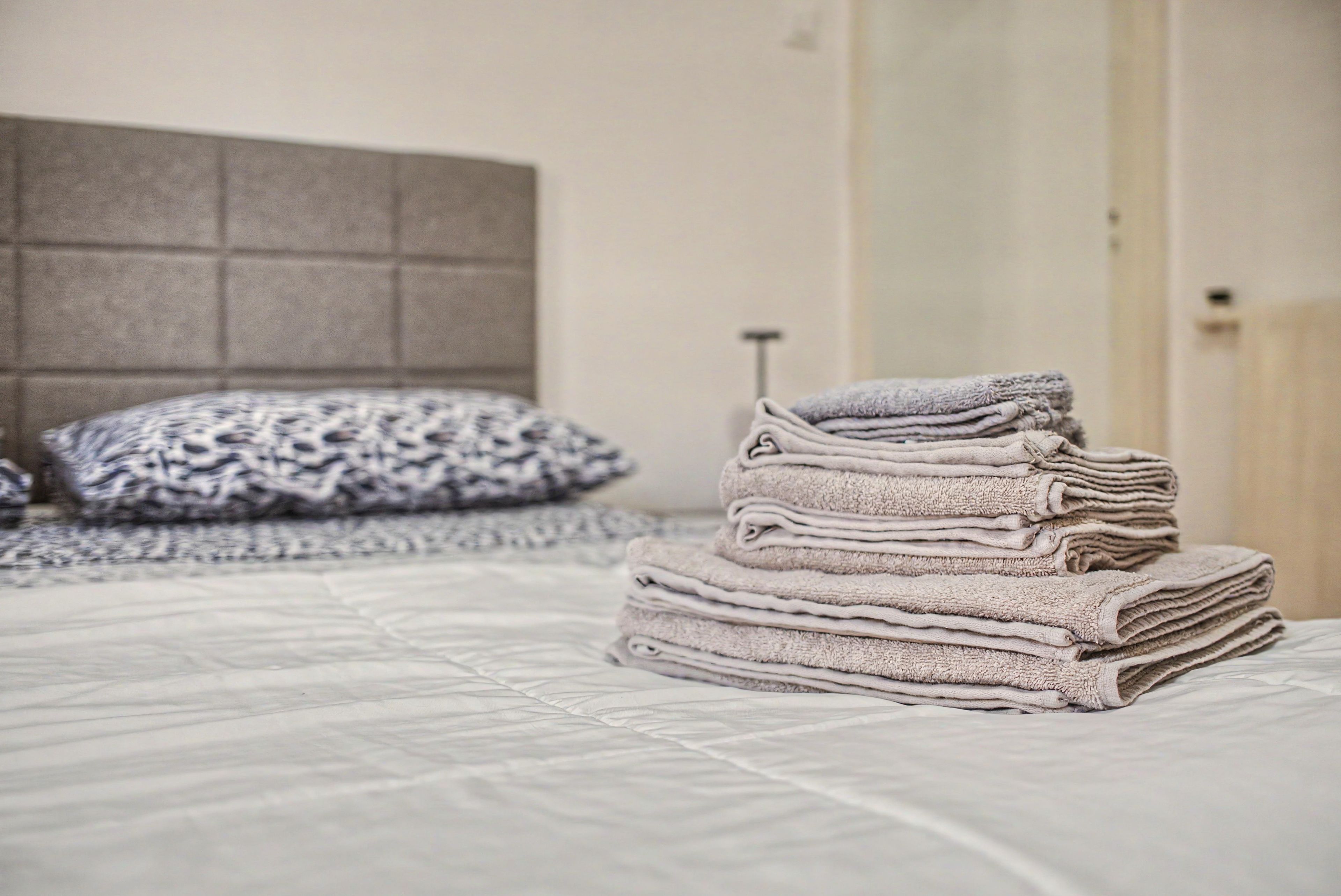 Un lit bien fait, avec un coussin à motifs et une pile de serviettes pliées.