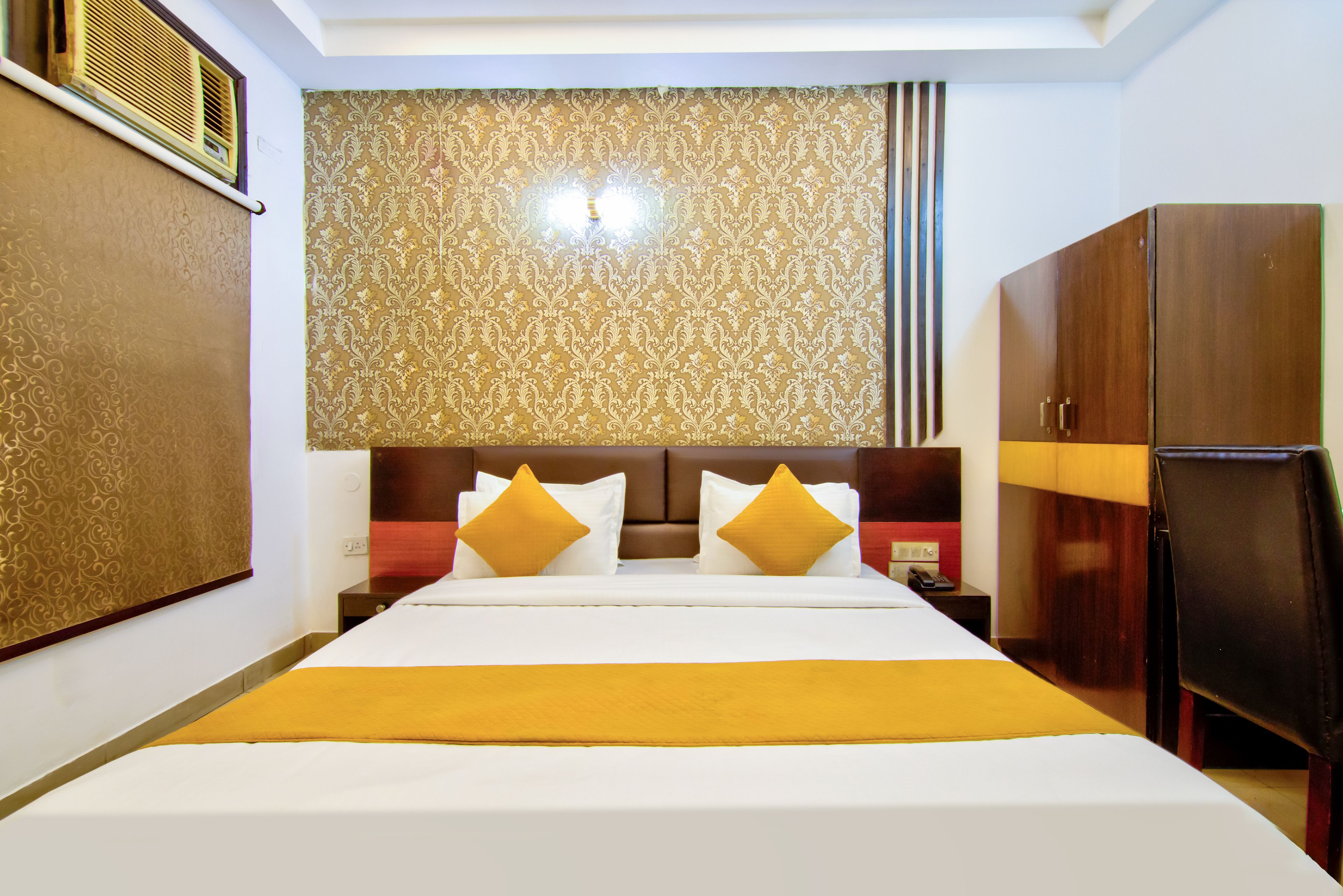 Una habitación de hotel con una cama grande, dos almohadas, una mesita de noche con lámpara, un armario y un panel decorativo en la pared.