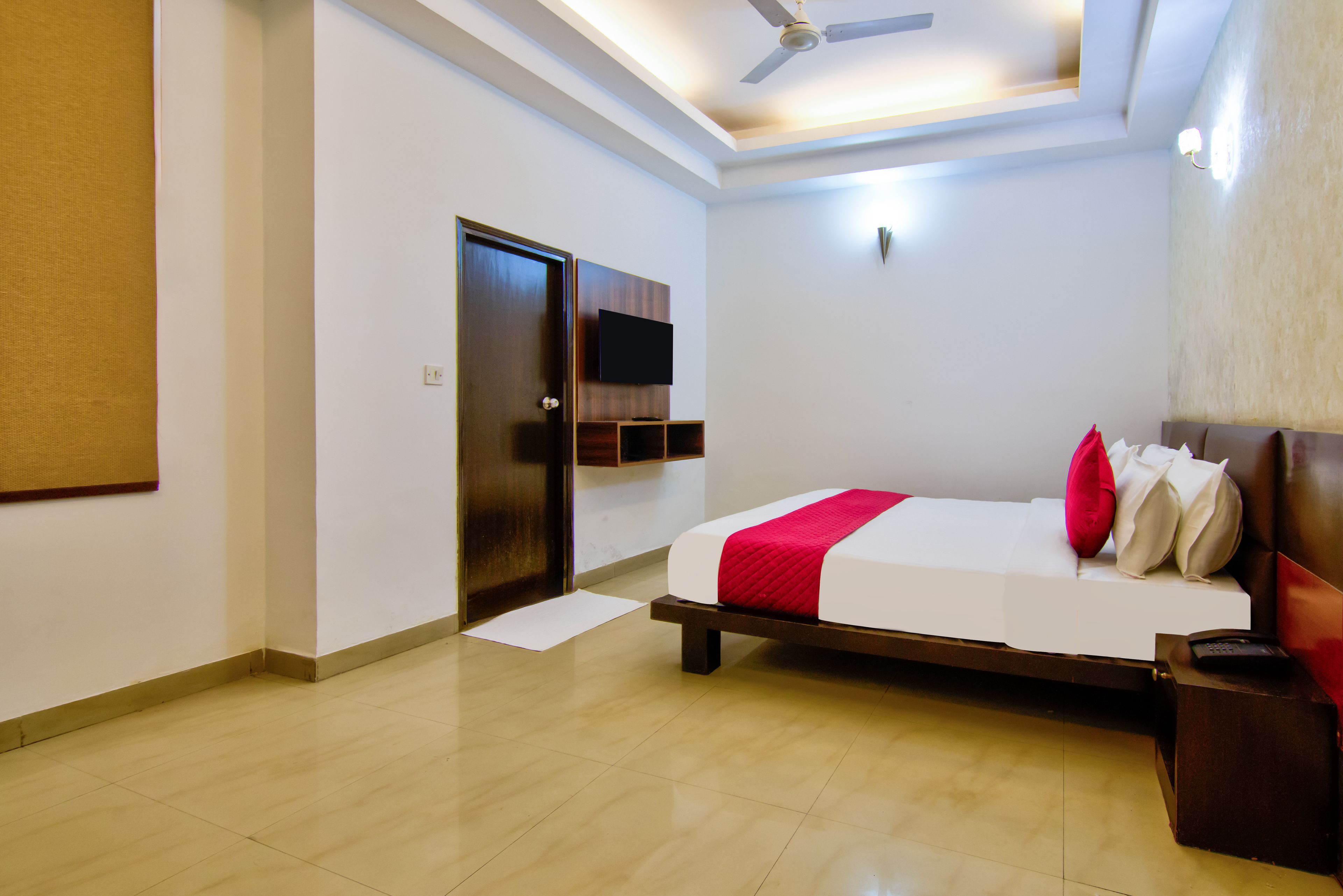 Habitación de hotel con cama, puerta, ventilador de techo y televisor de pantalla plana montado en la pared.